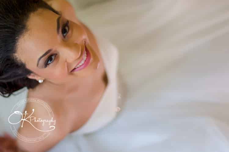 A smiling bride in a white dress looking up at the camera.