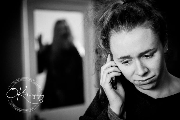 Woman talking on the phone with a worried expression, another person is blurred in the background.