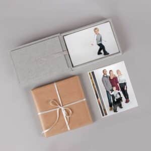 This image showcases a family portrait session, with a family of four standing close together and smiling at the camera. The image features fine art prints displayed in a dedicated box, with intricate details and textures visible.