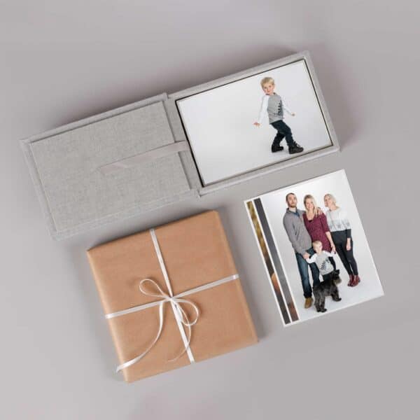 This image showcases a family portrait session, with a family of four standing close together and smiling at the camera. The image features fine art prints displayed in a dedicated box, with intricate details and textures visible.