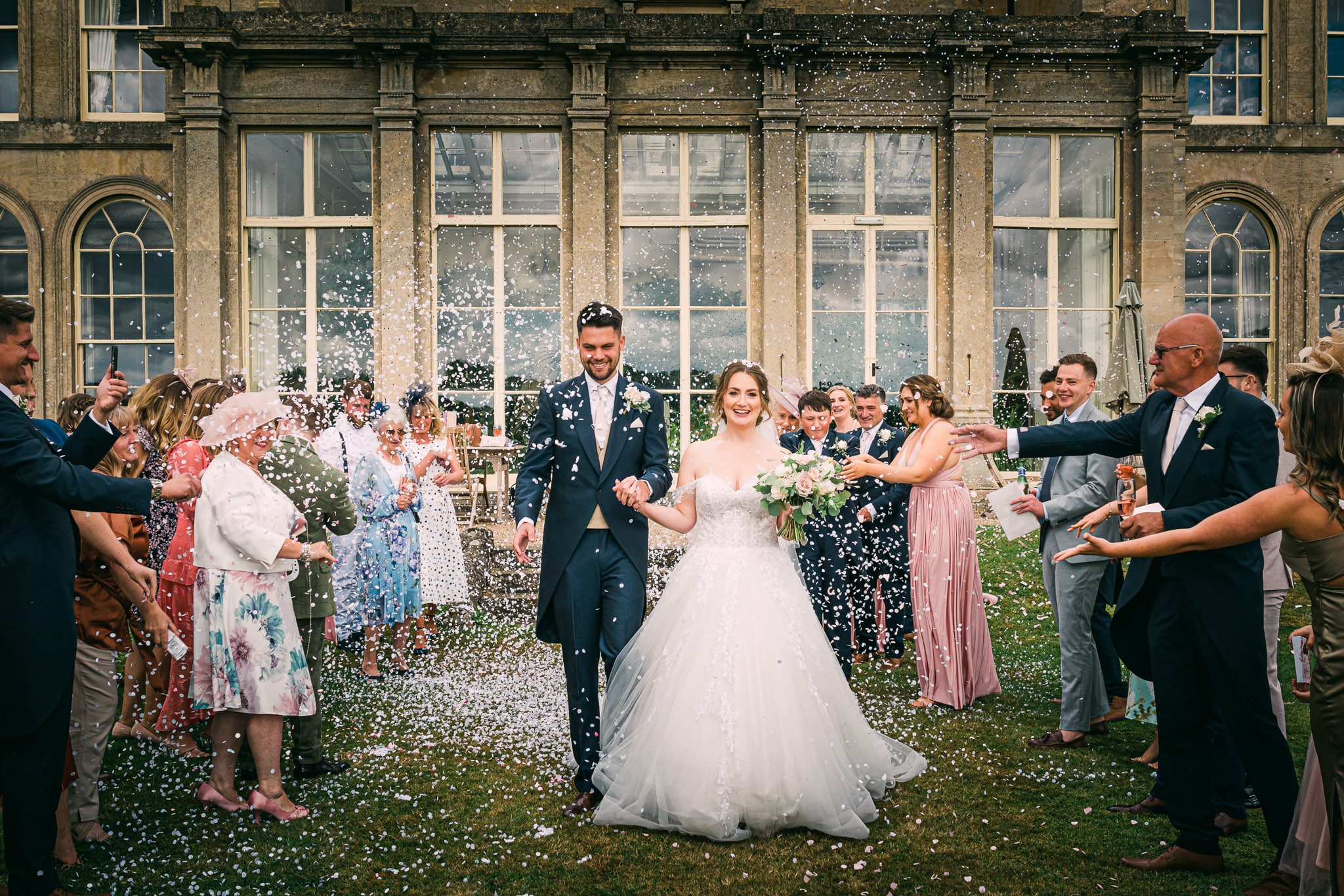 This wedding photography image shows the happy couple being showered with confetti by their loved ones at Prestwold Hall. The expertly-captured image showcases the joy and celebration of the couple's special day, with the confetti adding a touch of fun and whimsy to the scene. The photographer has expertly captured the moment, with the couple's love and joy shining through in every aspect of the photo.