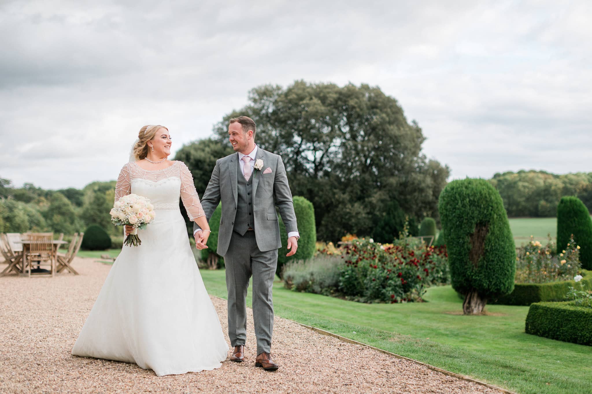 This wedding photography image captures the happy couple in a romantic pose in the gardens of Prestwold Hall. The lush greenery and beautiful flowers provide a stunning backdrop for the couple, who look radiant and in love. Our photographer has expertly captured the beauty of the surroundings, showcasing every detail of the scene in stunning clarity. This image is a beautiful testament to the love shared between the couple on their special day.