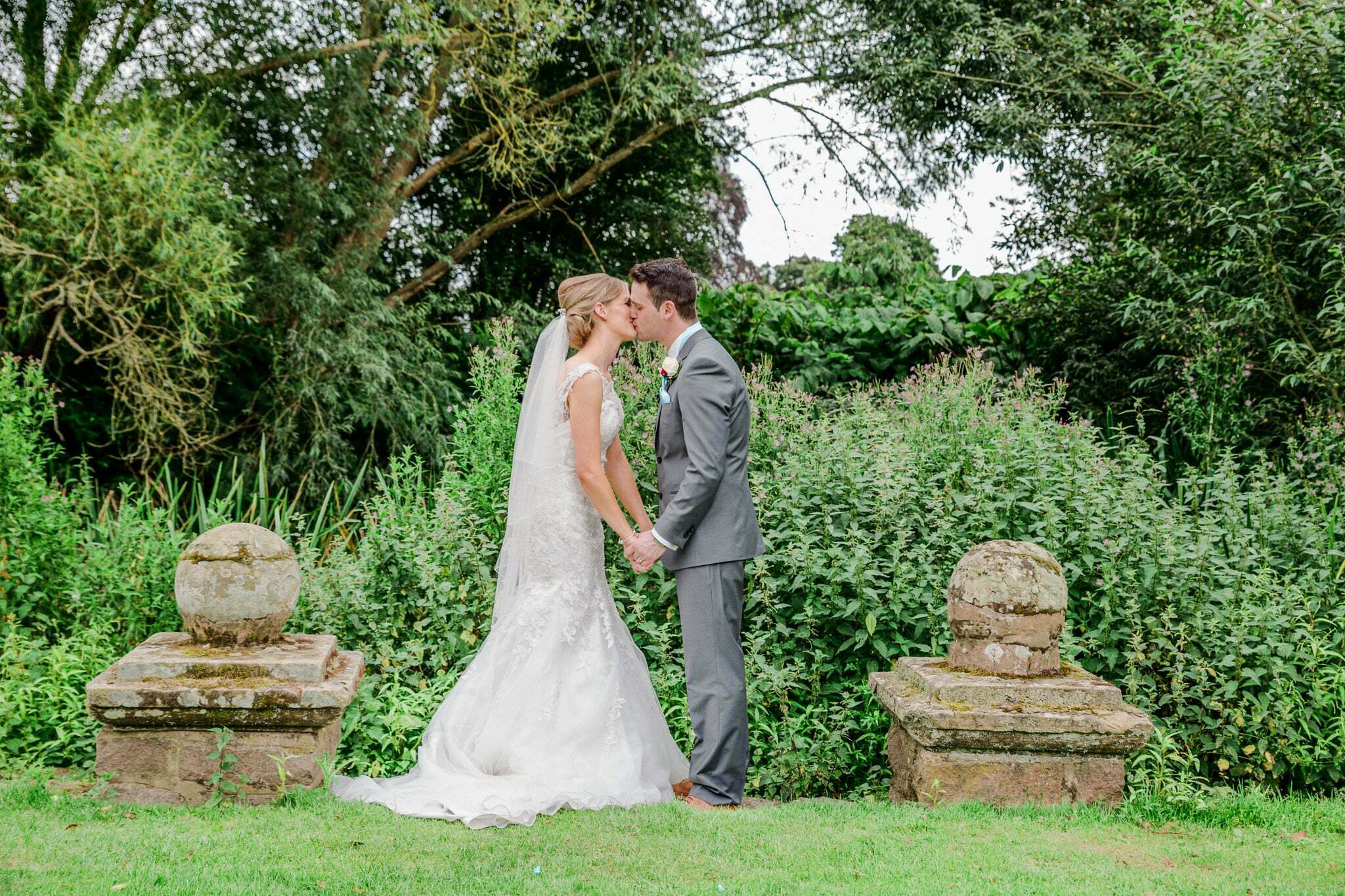 A bride and groom standing in front of Rothley Court Hotel on their wedding day, with the bride in a white wedding gown and the groom in a suit, looking happy and in love.