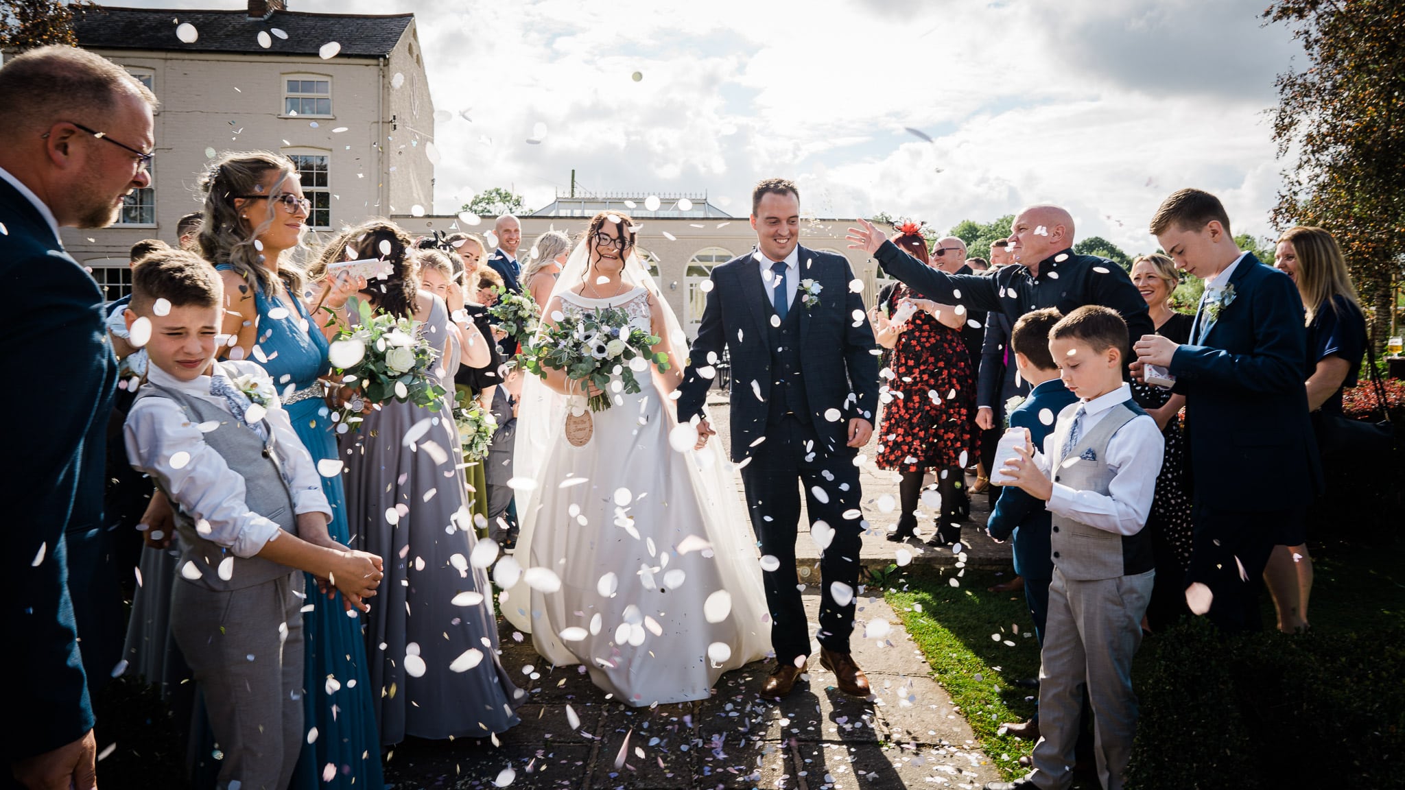 Bride and groom walking through a confetti tunnel at Shearsby Bath wedding venue, surrounded by friends and family.