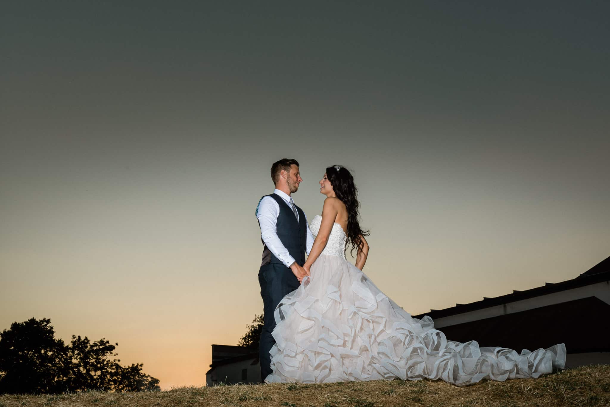 A bride and groom are embracing each other in front of a beautiful sunset at Sketchley Grange Hotel.