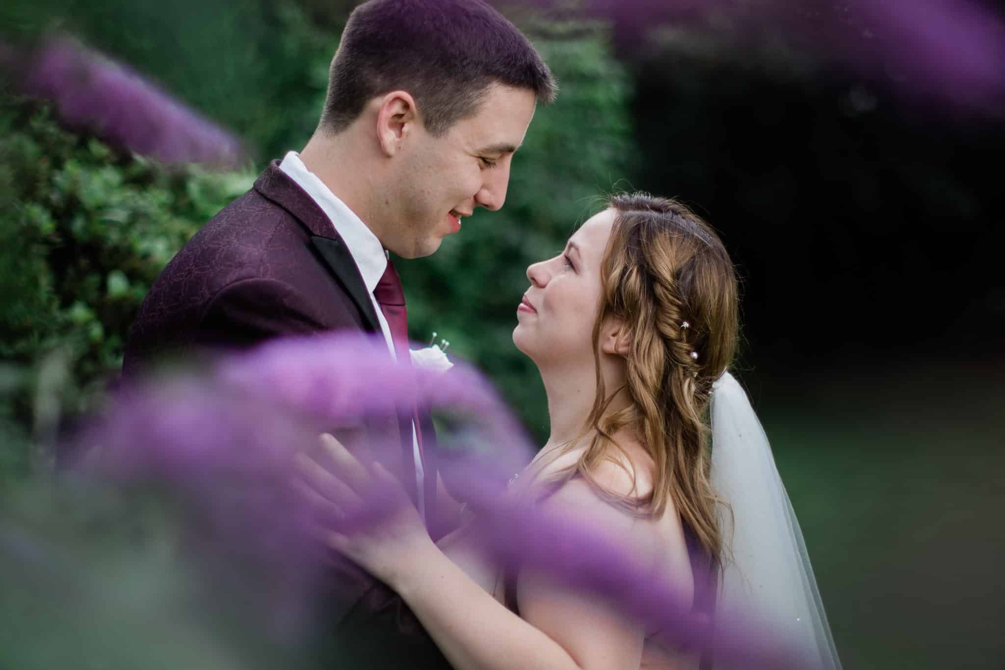 Bride and groom share a romantic moment at Sketchley Grange Hotel, with the hotel in the background and a blurred flower in the foreground.