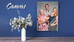 A canvas print of a family portrait on a blue wall next to a vase with eucalyptus branches.