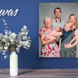 A canvas print of a family portrait on a blue wall next to a vase with eucalyptus branches.