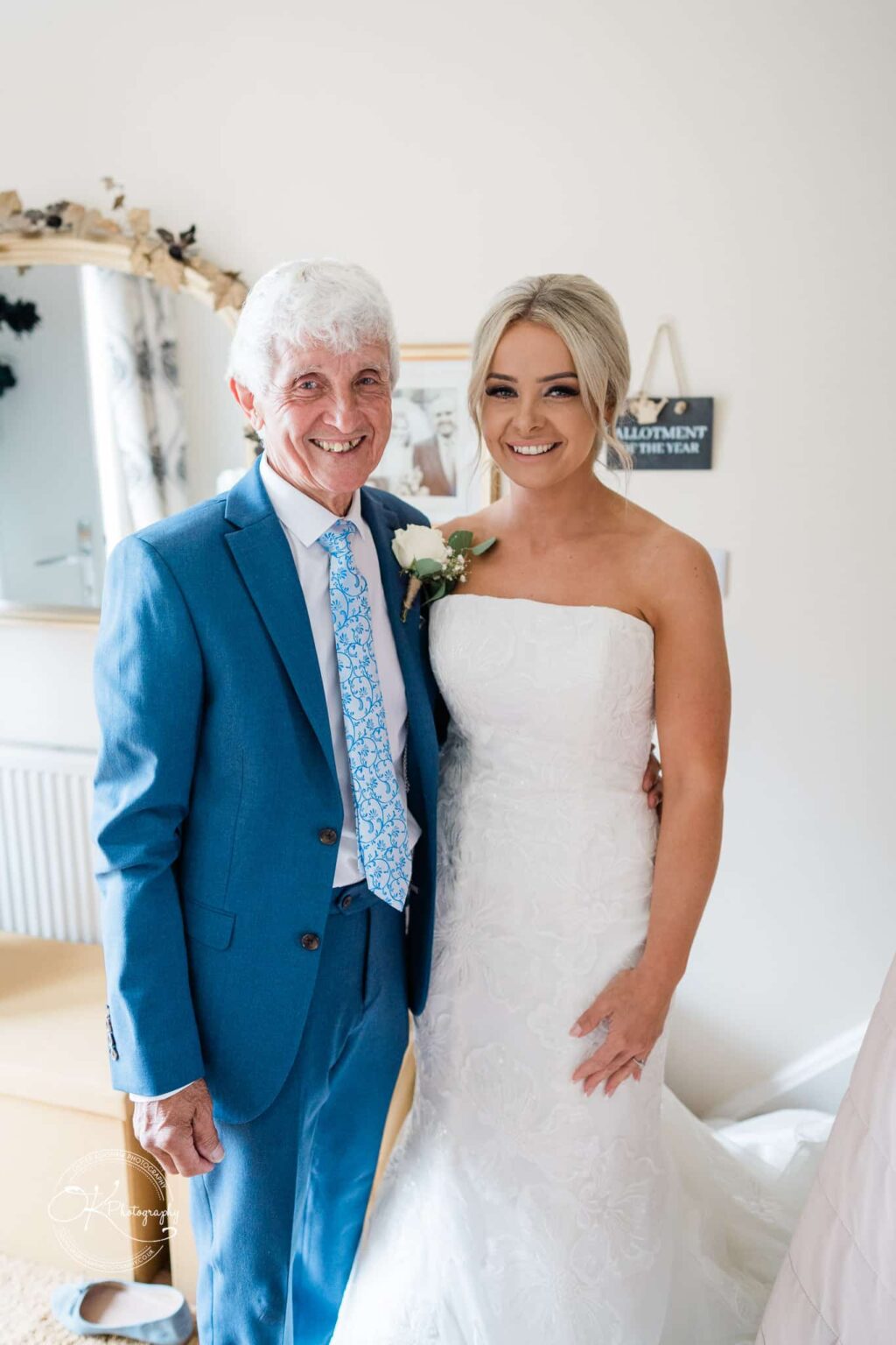 Bride in a white wedding dress posing with an older man in a blue suit and patterned tie.