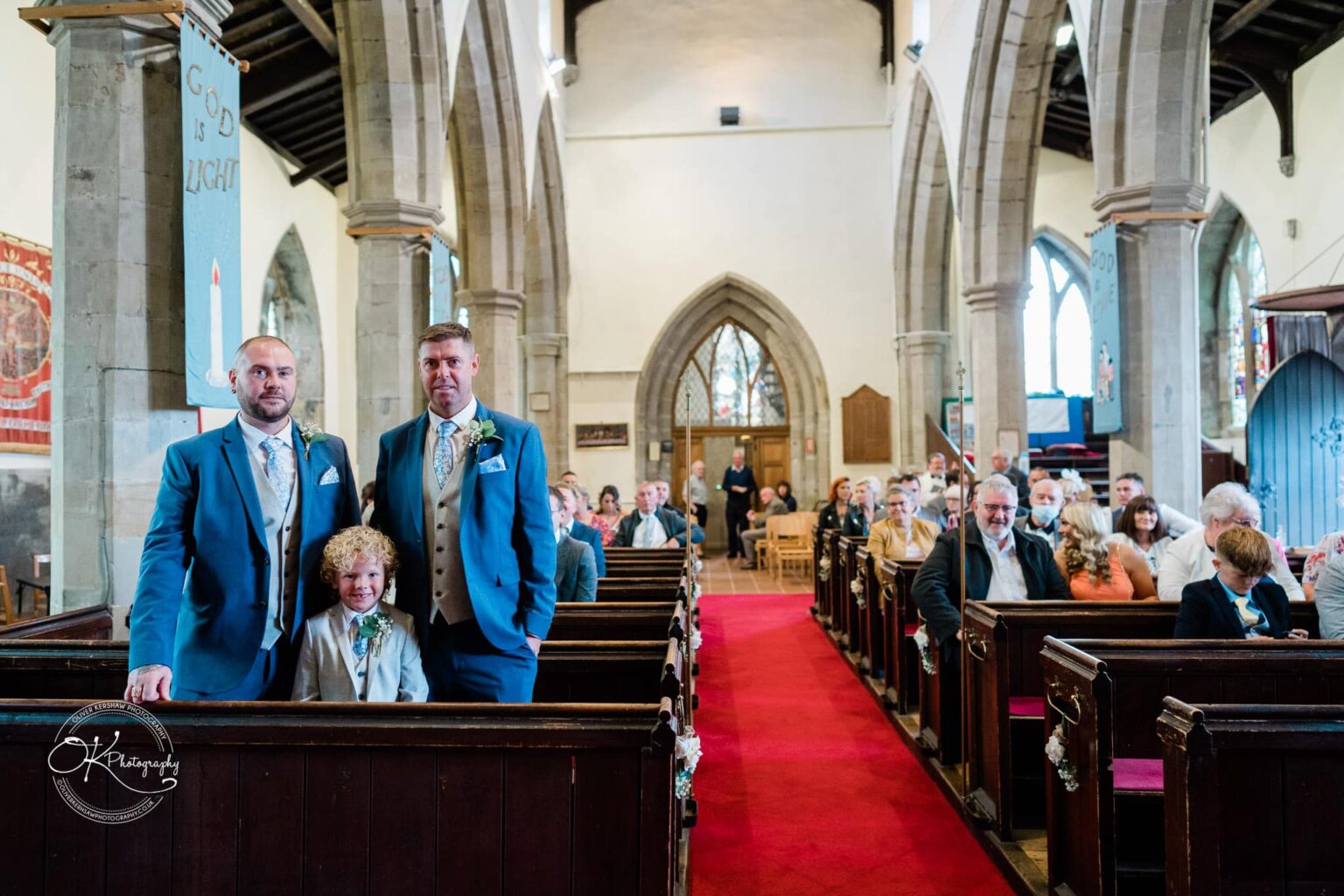 Two men and a child in blue suits posing in the aisle of a church with a red carpet, surrounded by pews filled with people.