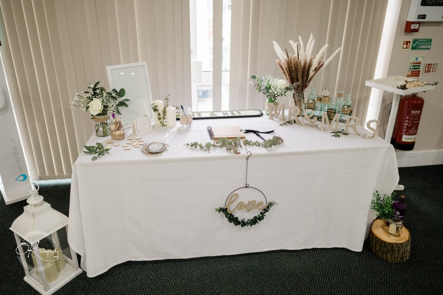 A beautifully decorated wedding table with various items, including wooden "Mr & Mrs" letters, a small sign reading "love", flowers, candles, a guestbook, a photo frame, and other rustic decor elements.