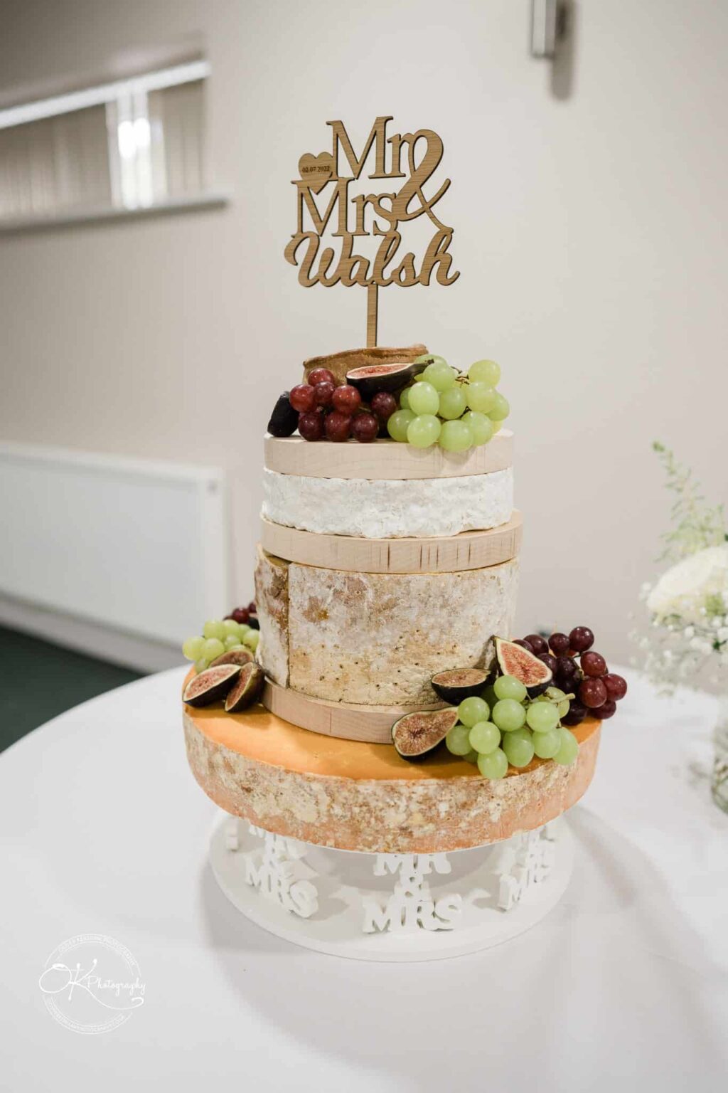 Wedding cheese cake decorated with grapes and figs, topped with a "Mr & Mrs Walsh" sign.