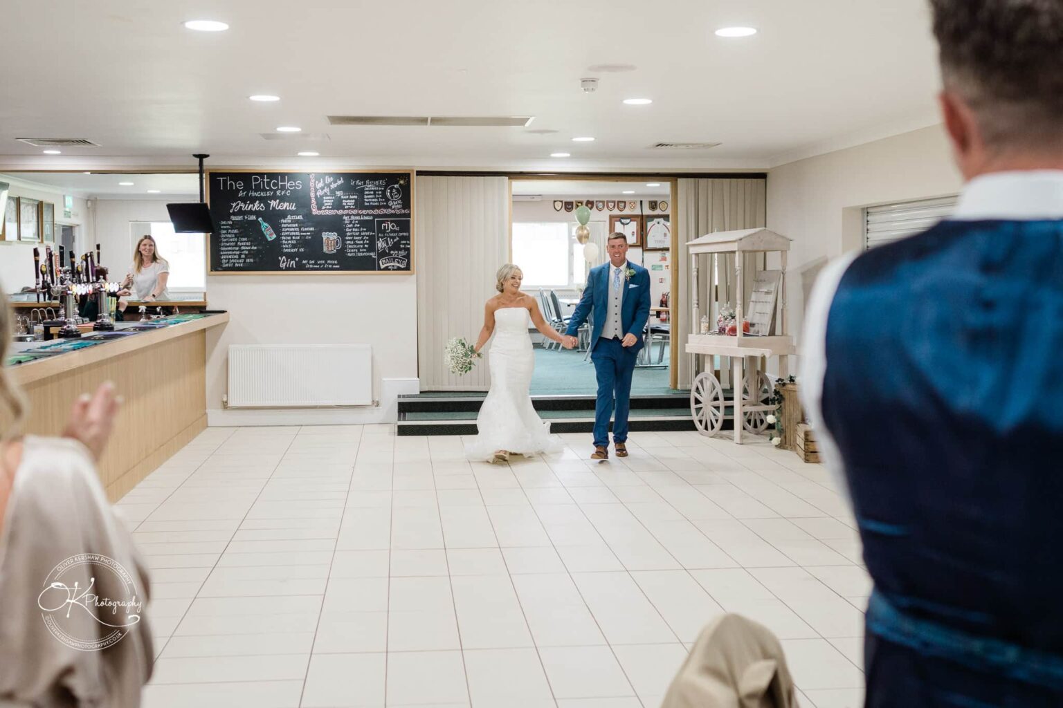 Bride and groom entering a reception venue, holding hands and smiling.