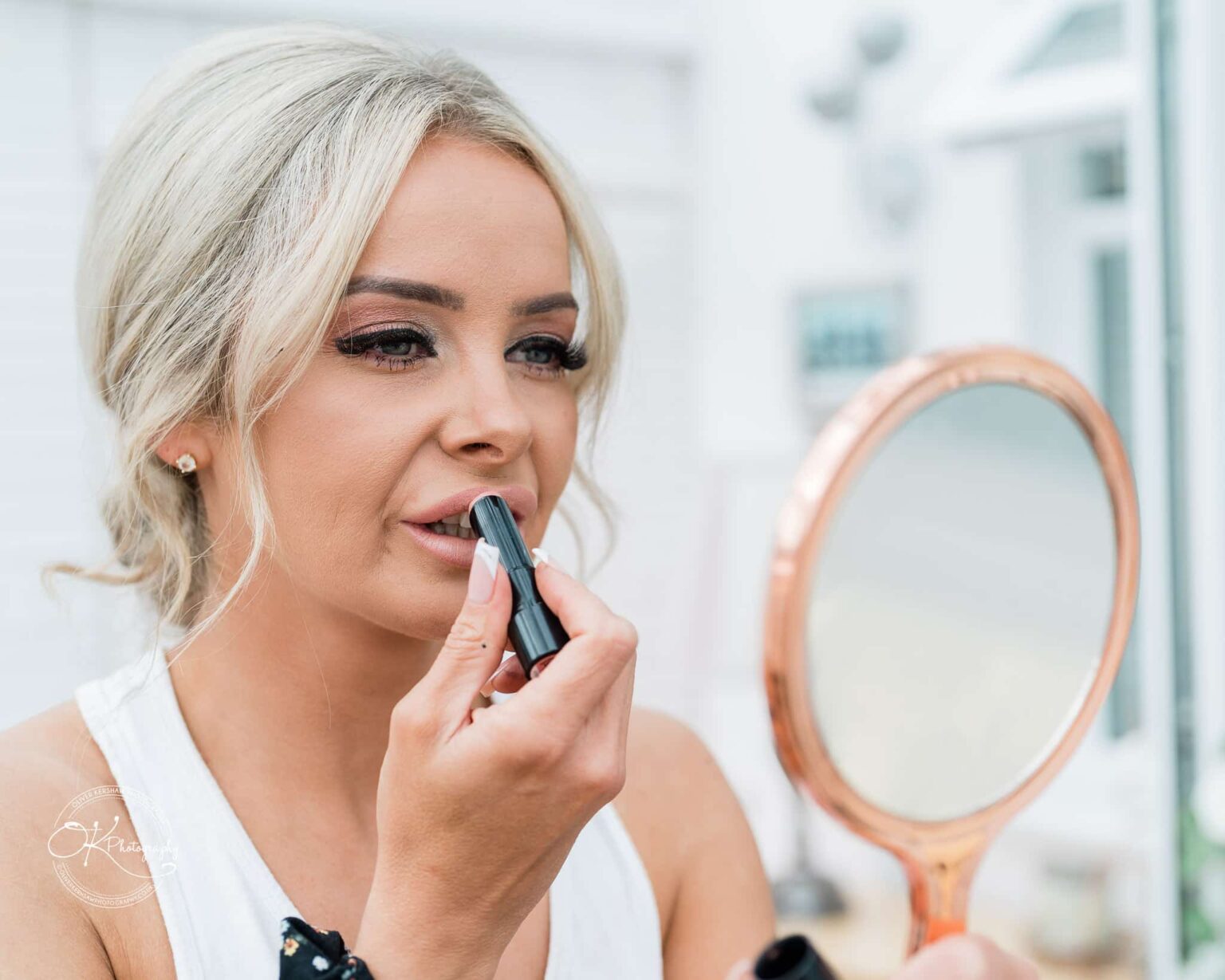 Woman applying lipstick while looking into a handheld mirror.