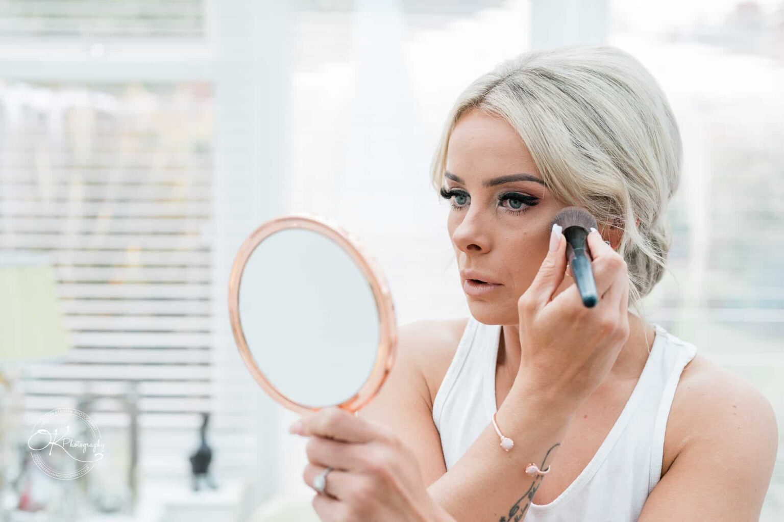 Woman applying makeup while holding a round mirror.