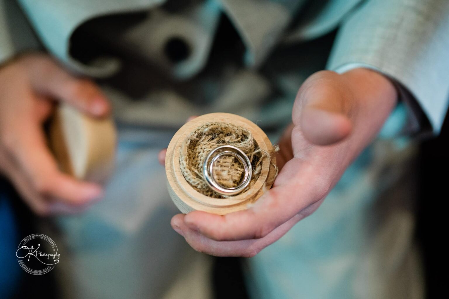 Hands holding a wooden ring box with two silver rings inside.