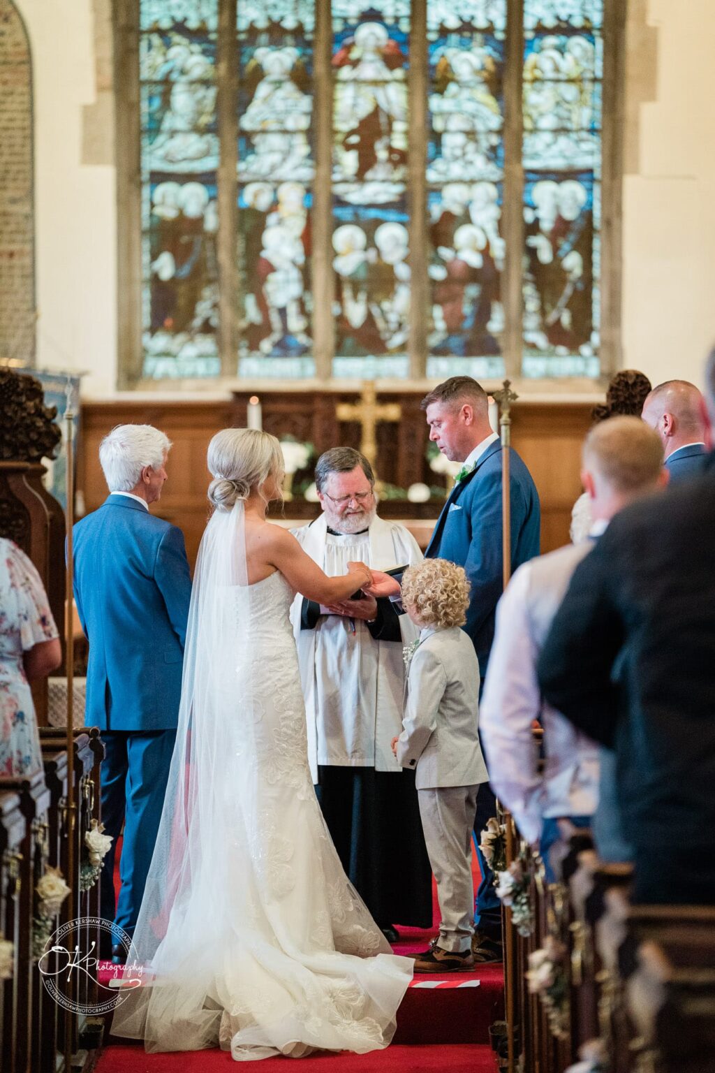 Bride and groom exchanging vows at the altar in a church, officiated by a priest with guests seated in pews.