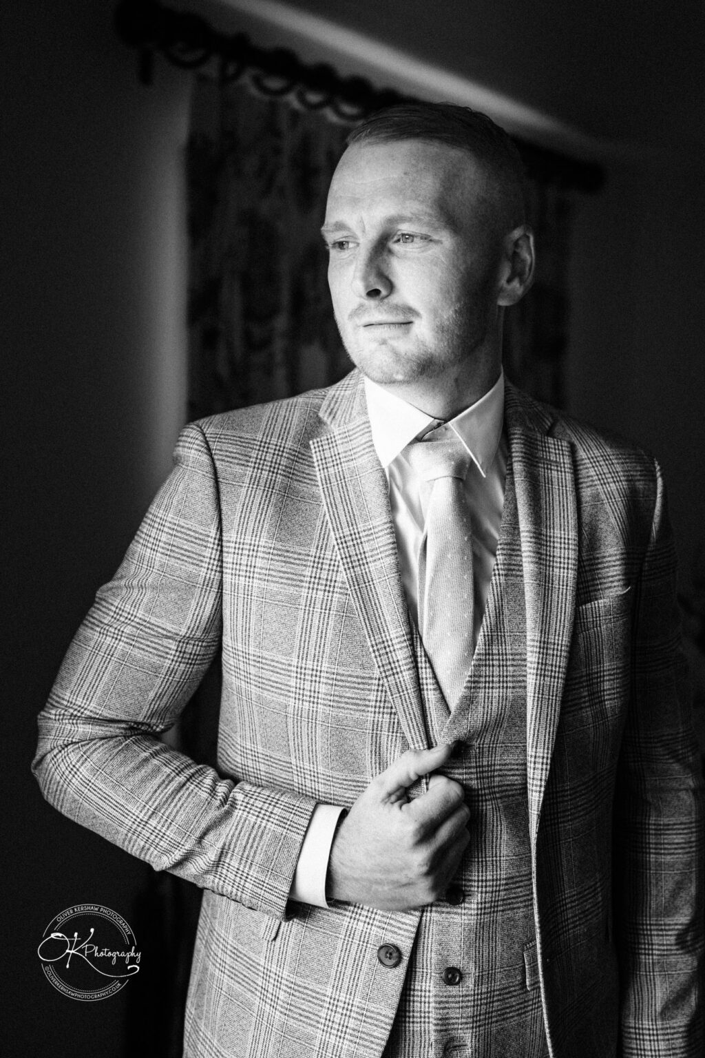 A man in a checked suit looks off-camera with a serious expression, in black and white.