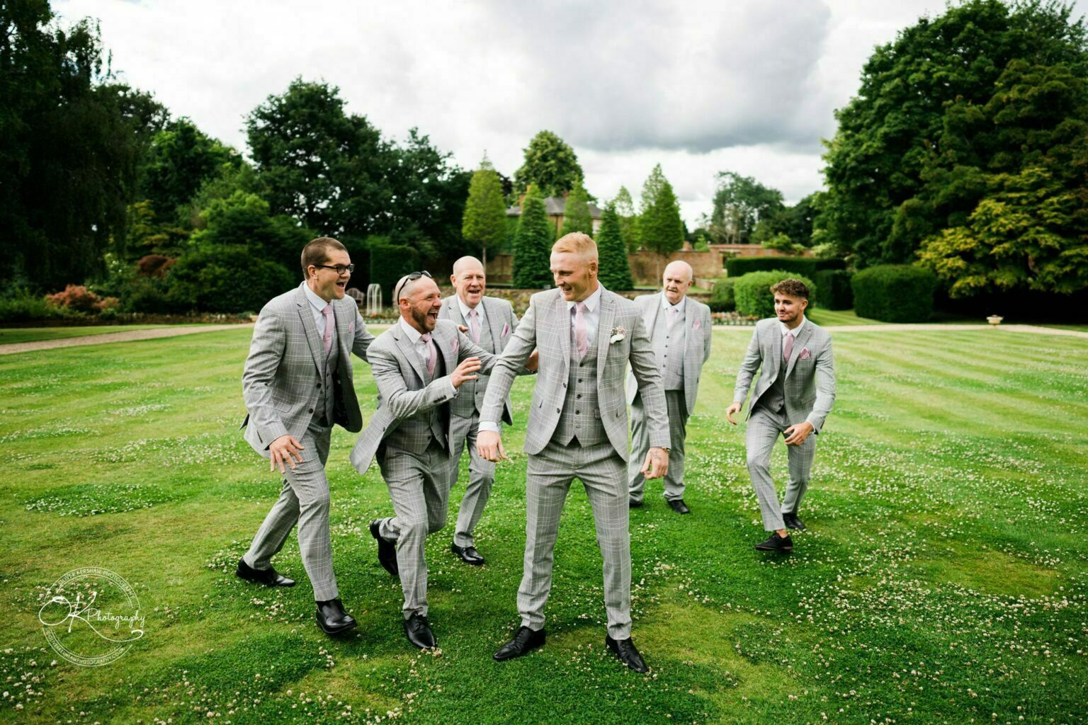 Groom and groomsmen in grey suits playing on grassy grounds at Bourton Hall.