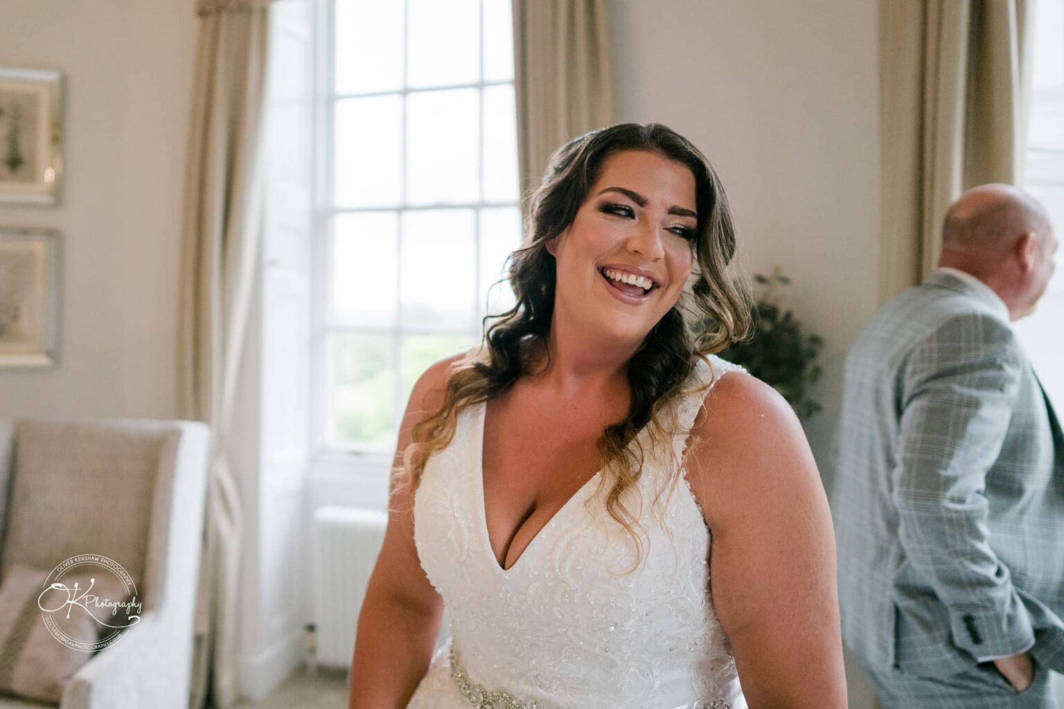 Bride smiling in a wedding dress with a man in a suit jacket in the background at Bourton Hall.