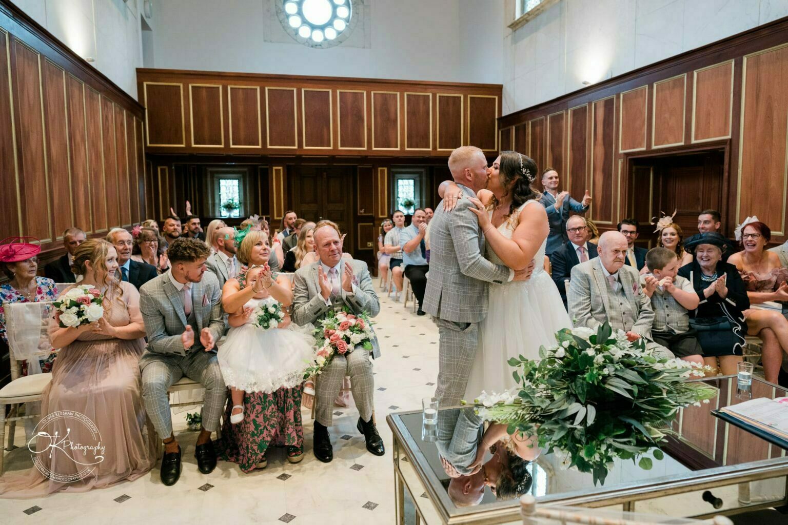 Bride and groom kissing in a hall with guests applauding.