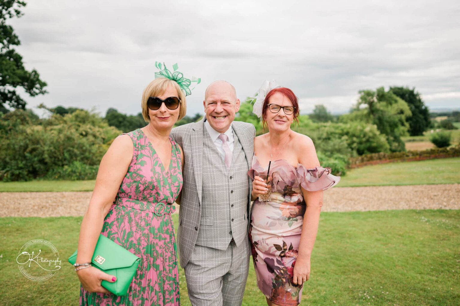 Three people in colourful outfits smiling at a wedding in an outdoor setting at Bourton Hall.