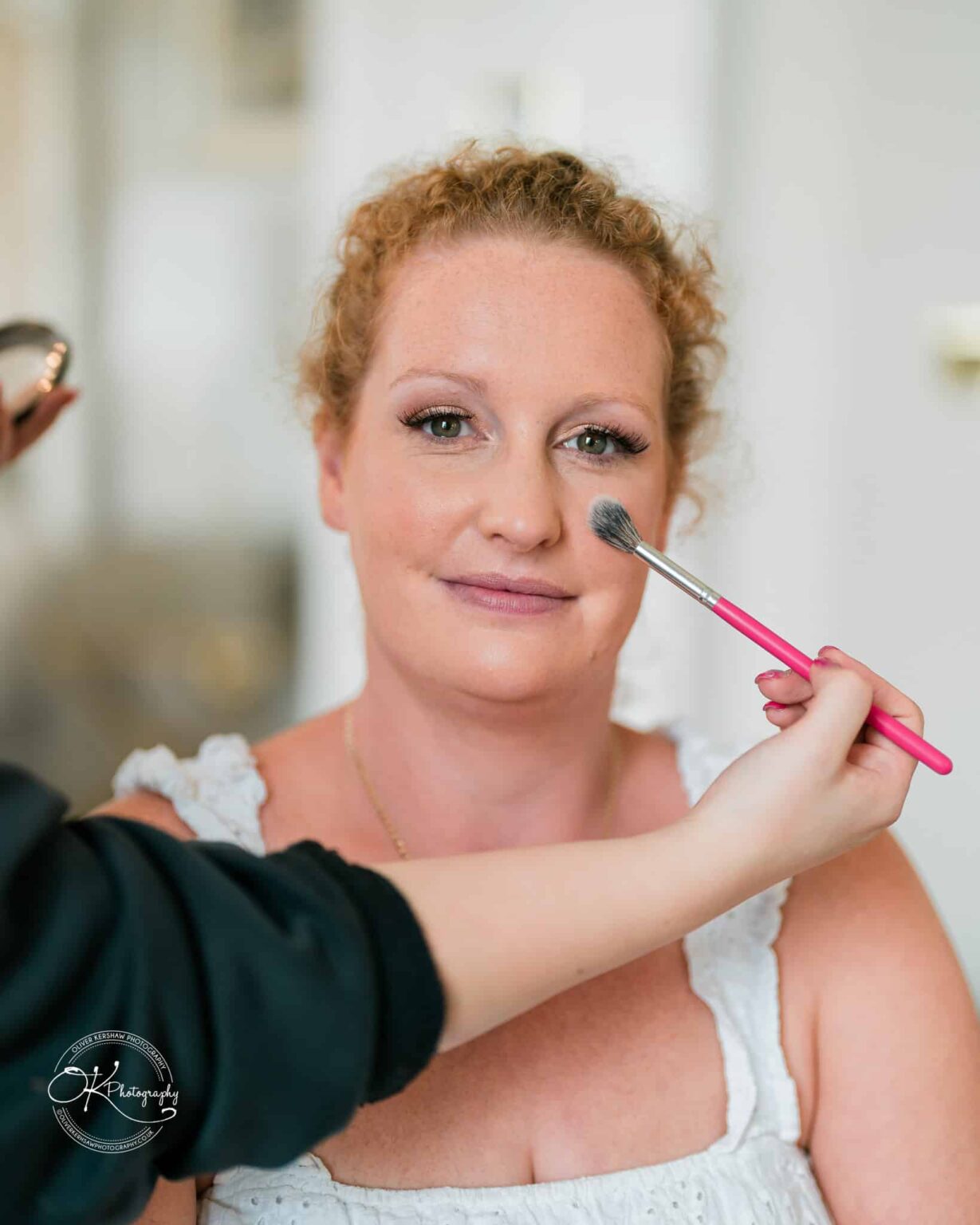 Person having makeup applied with a brush during wedding preparations.