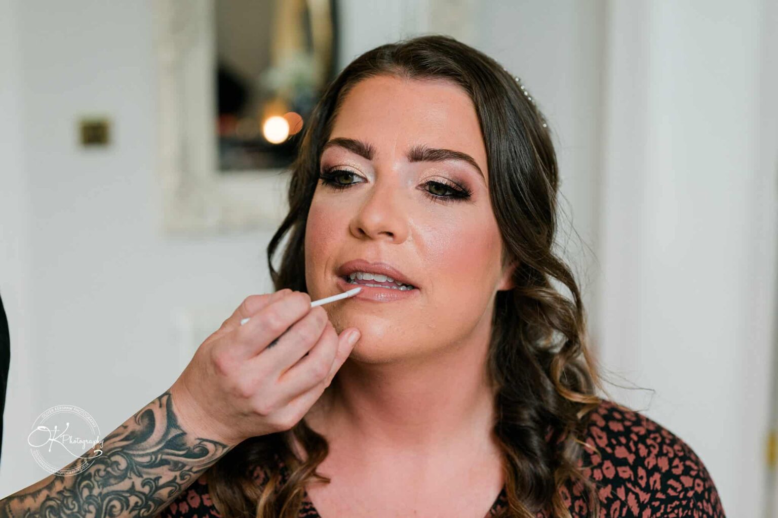 A bride having her makeup applied, focusing on her lips, before her wedding at Bourton Hall.