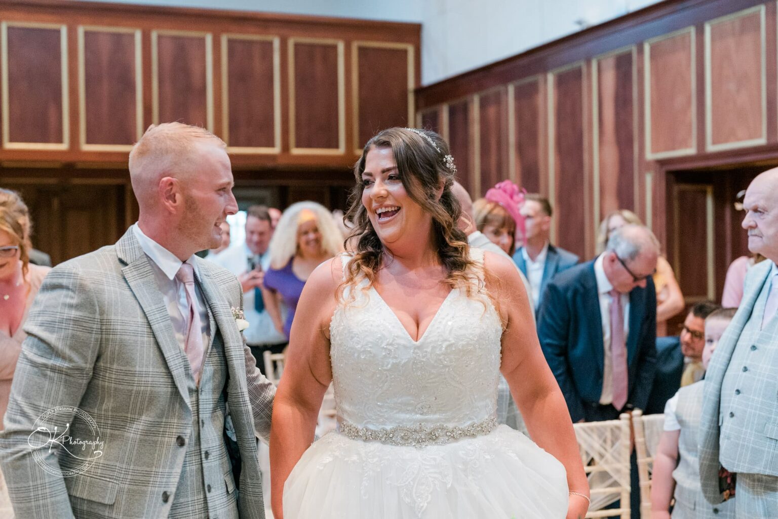 Bride and groom smiling at each other during their wedding ceremony at Bourton Hall, surrounded by guests.