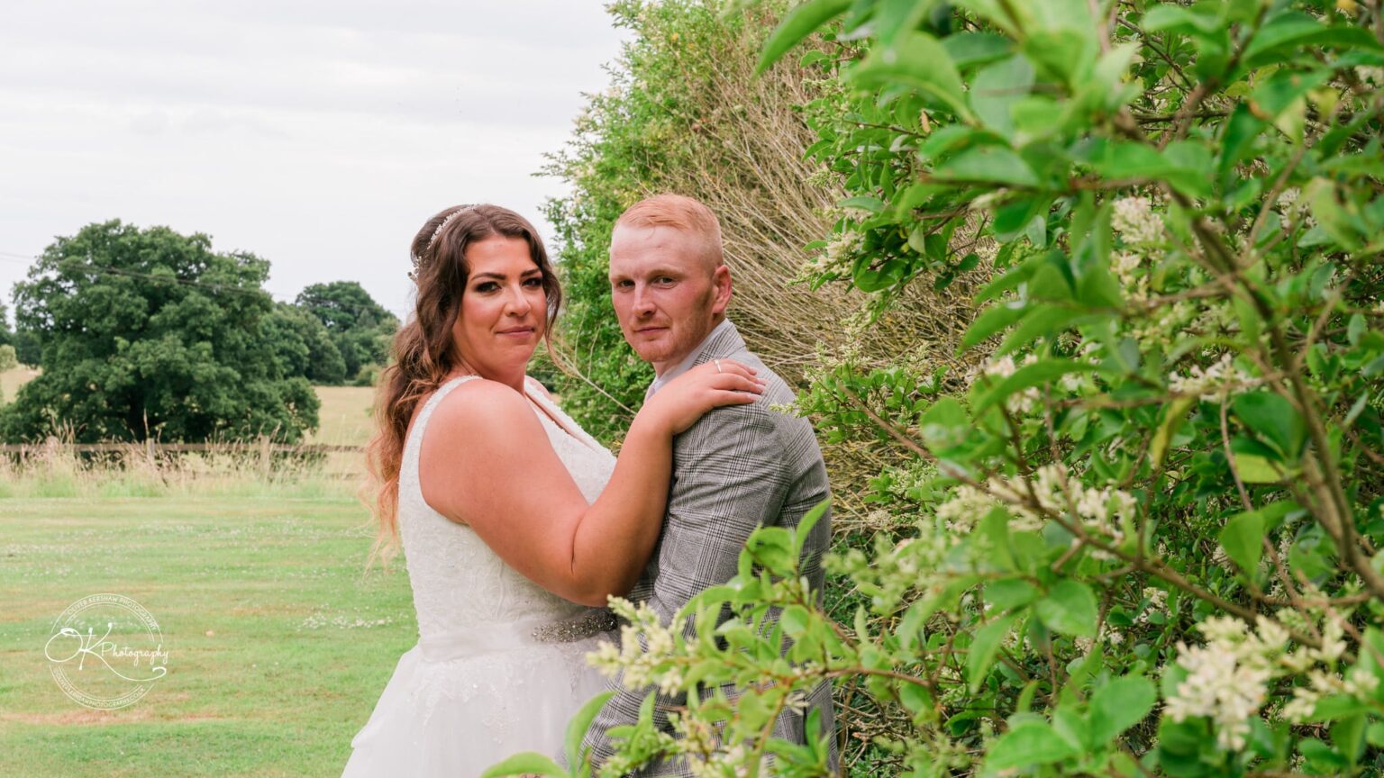 A bride and groom pose outdoors amidst greenery at Bourton Hall.