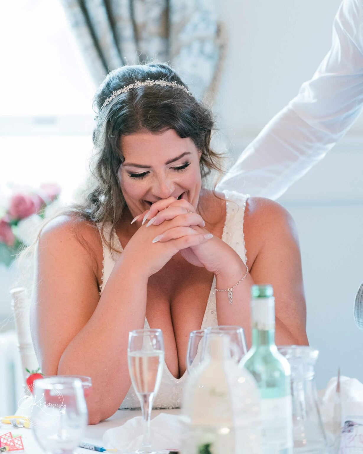 Bride laughing with clasped hands at a wedding reception table in Bourton Hall.