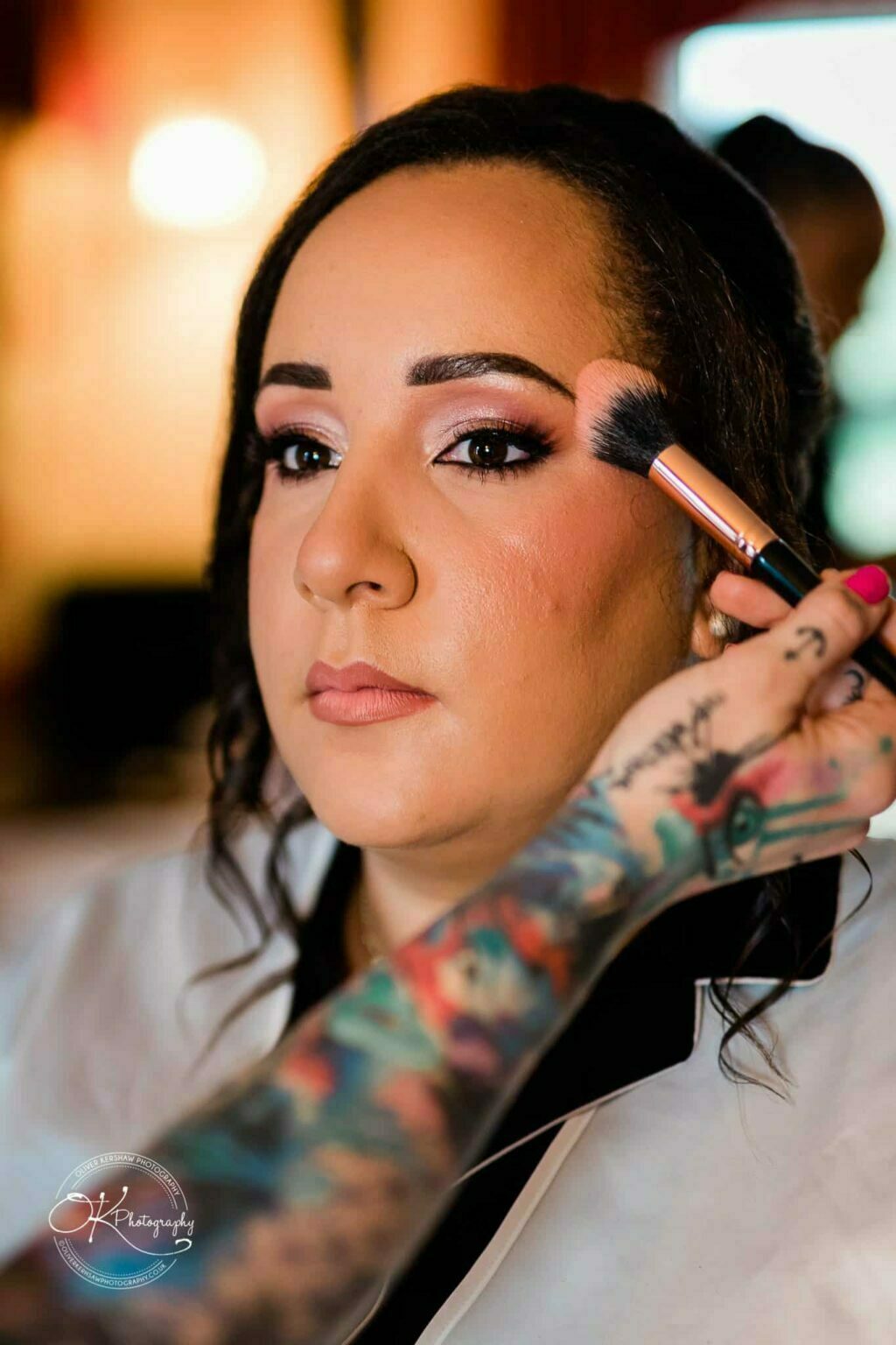 Brooksby Hall Wedding Photography A woman getting her makeup done, with a brush applying blush to her cheek.