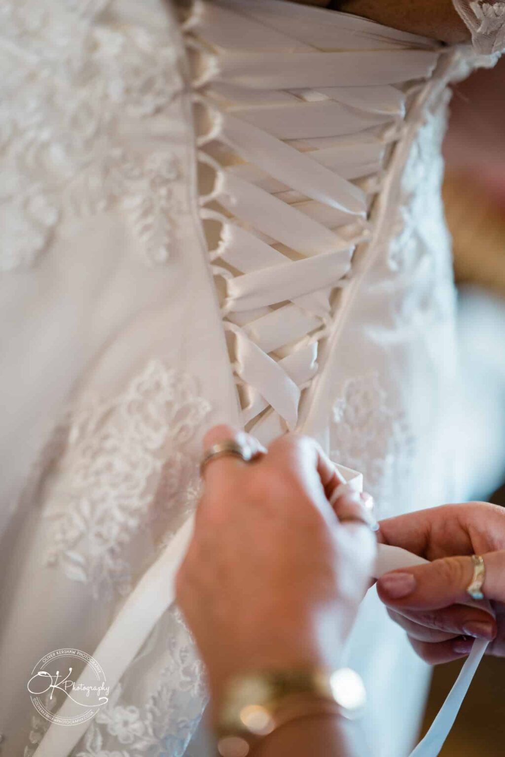 Brooksby Hall Wedding Photography Close-up of hands lacing up the ribbon back of a white lace wedding dress.