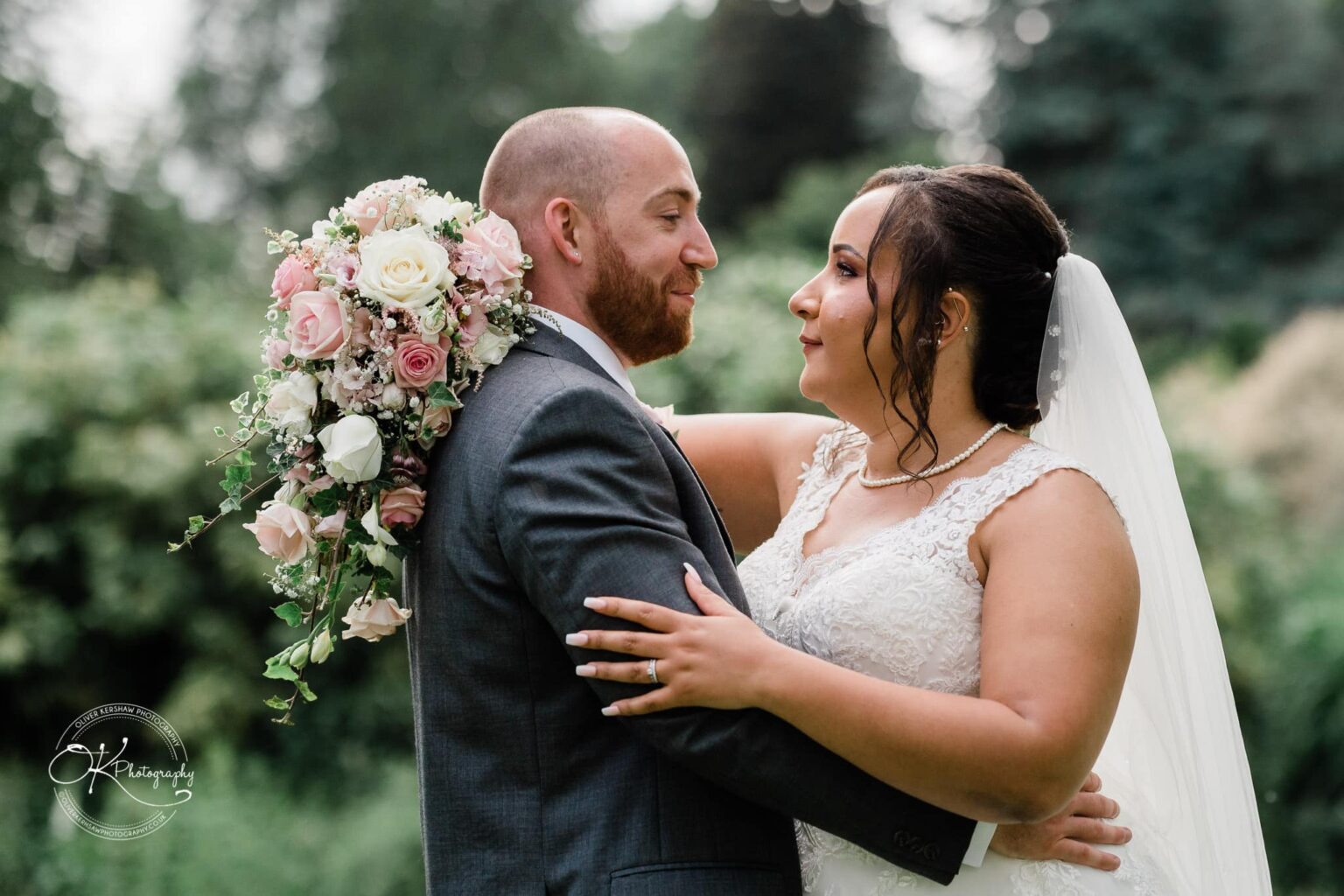 Brooksby Hall Wedding Photography Bride and groom embracing outdoors, the groom holds a pastel-coloured bouquet over his shoulder.