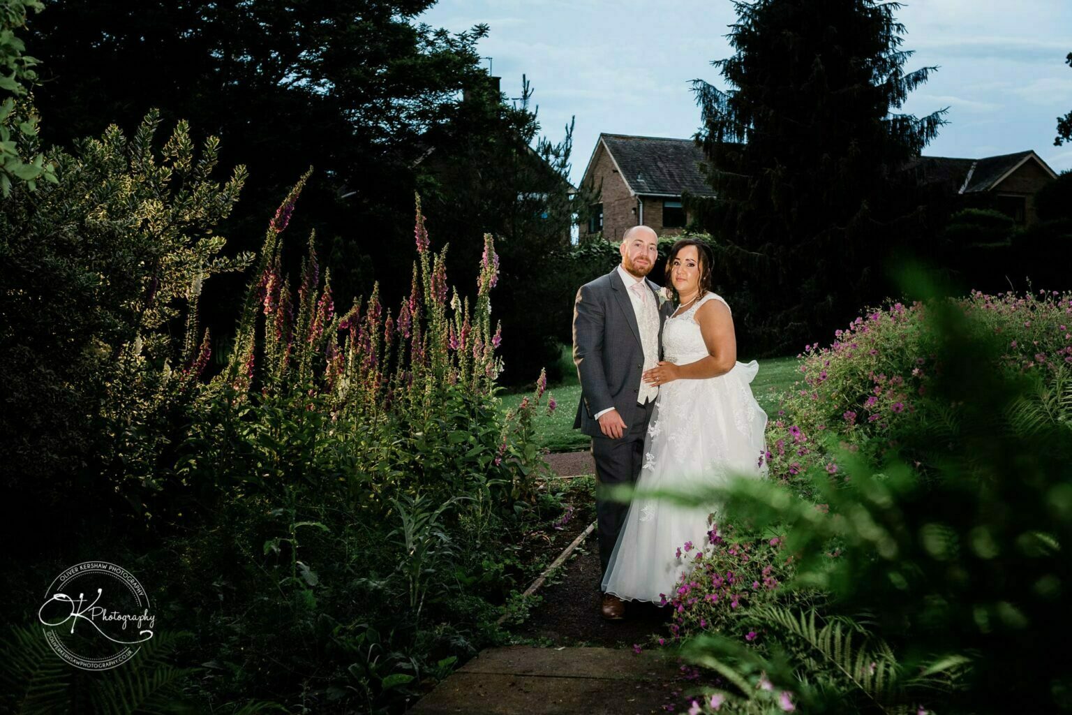 Brooksby Hall Wedding Photography A bride and groom posing outdoors in a garden with lush greenery and purple flowers at Brooksby Hall.