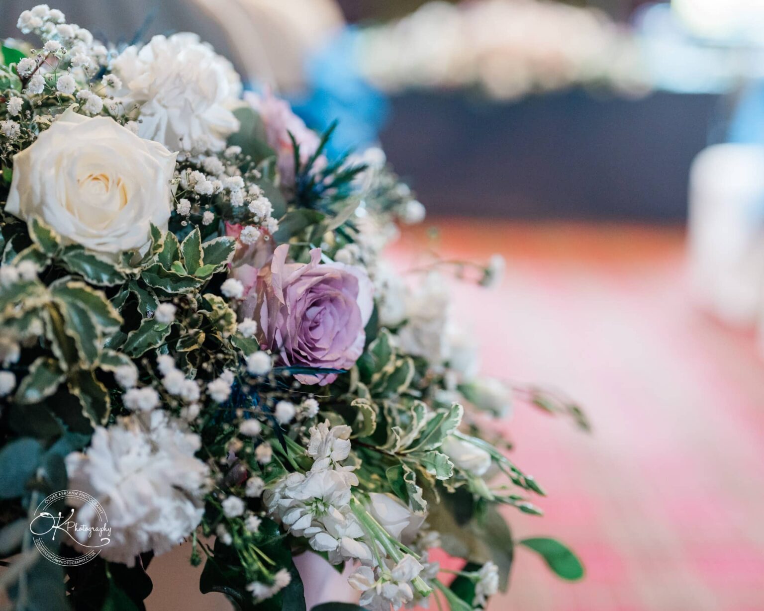 Close-up of a floral arrangement with white and lilac roses, baby's breath, and green foliage.