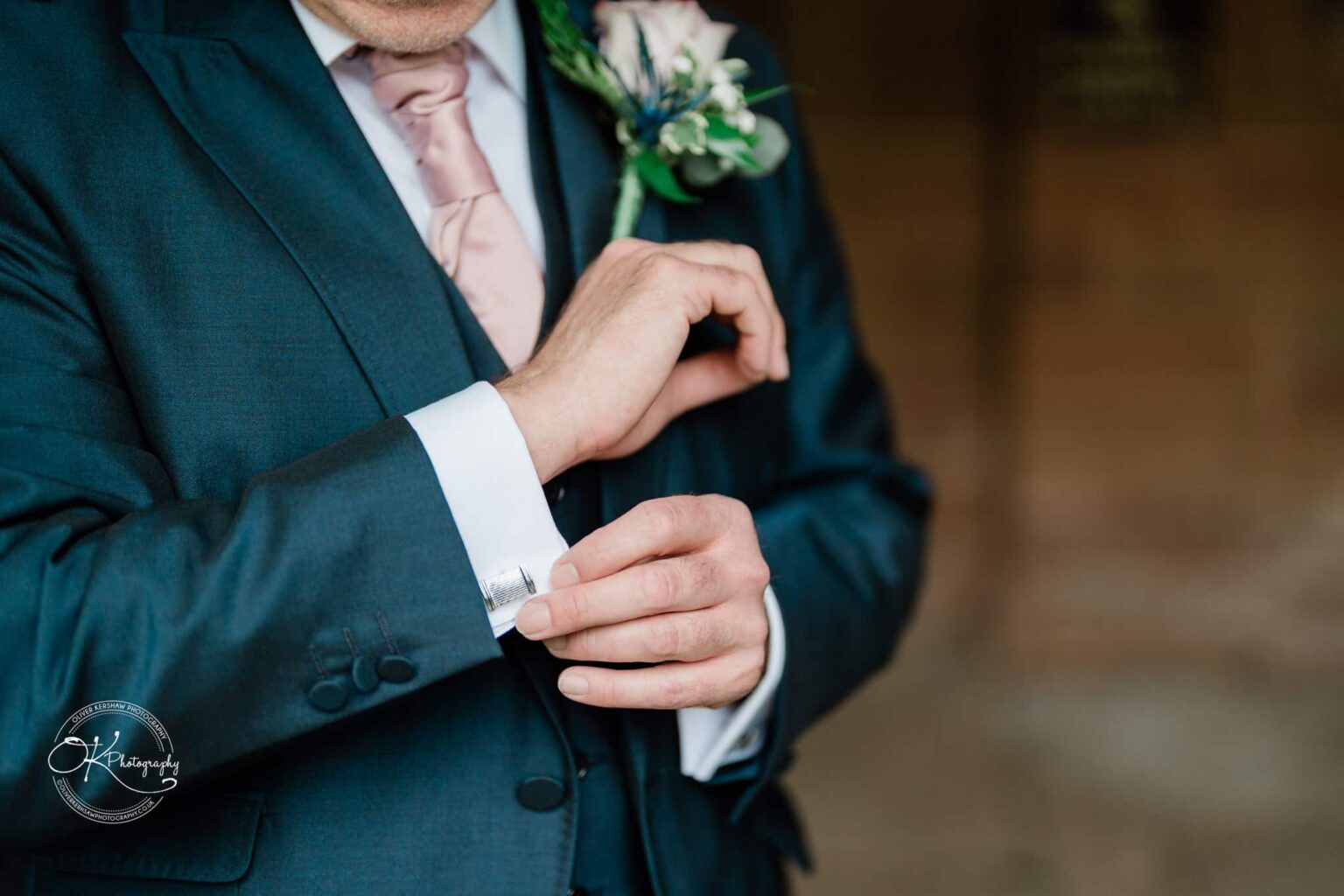 A man in a suit adjusting his cufflinks, wearing a boutonniere.
