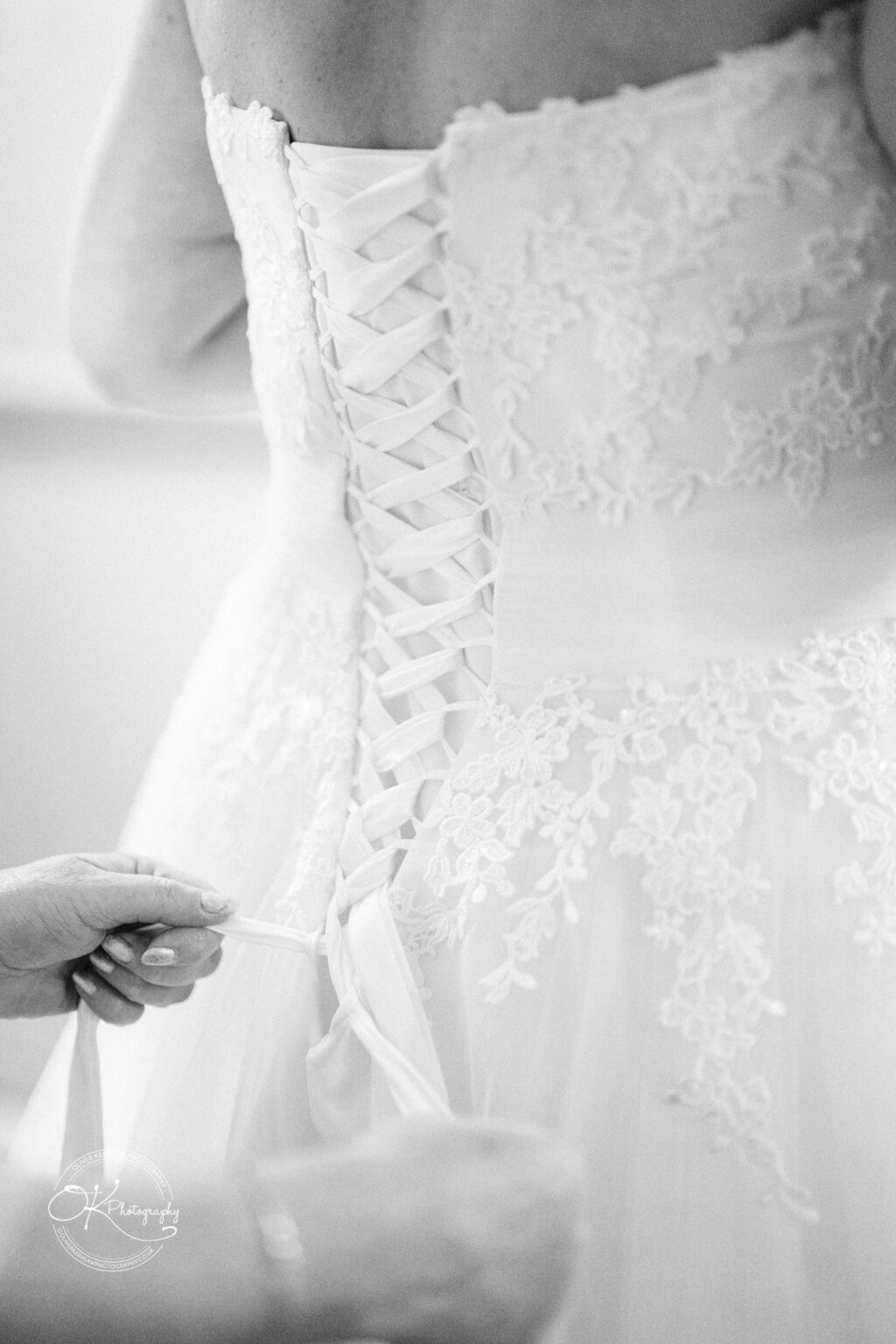 A close-up of someone tying the lace-up back of a white lace wedding dress.