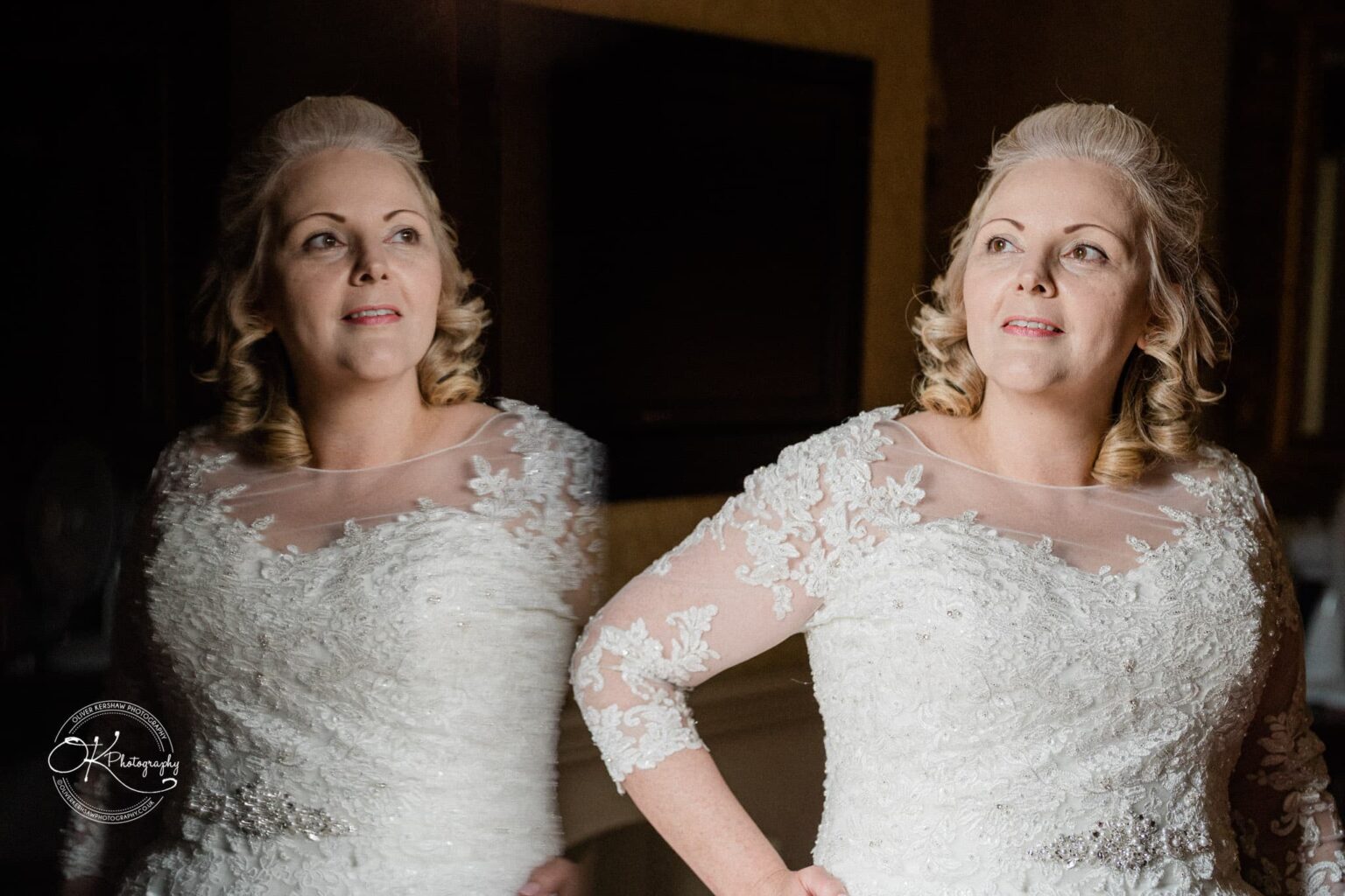 A bride in a white lace wedding dress is looking at her reflection in a mirror.
