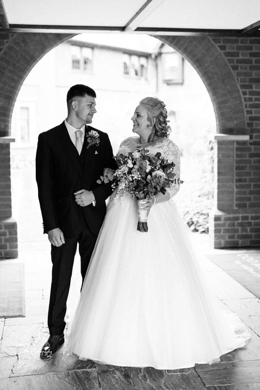 Bride and groom smiling at each other under an archway at Coombe Abbey Hotel.