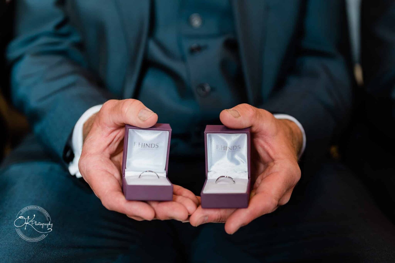 Person holding two ring boxes with rings inside, branded F.Hinds.