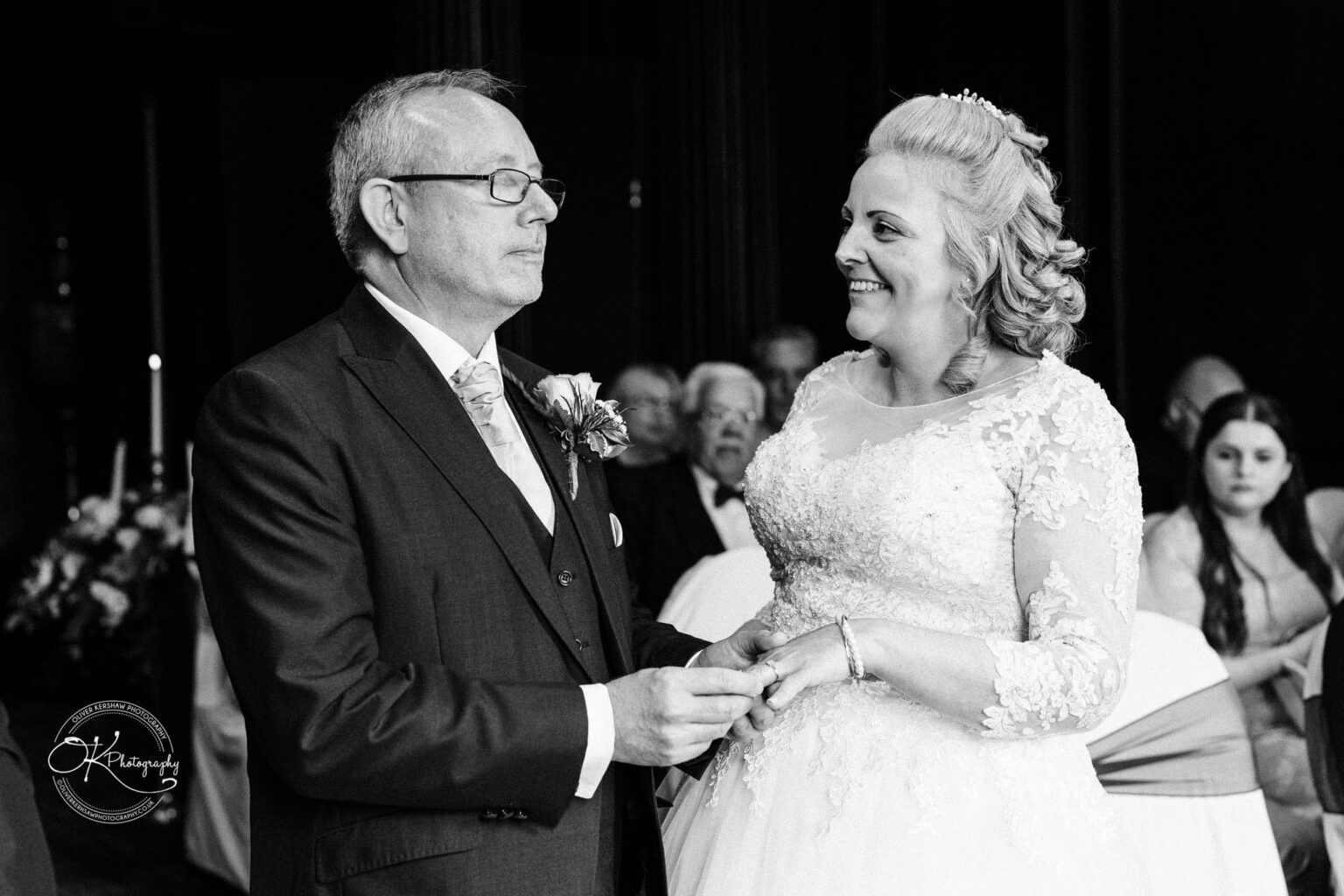 Bride and groom exchanging rings during their wedding ceremony, smiling and looking at each other.