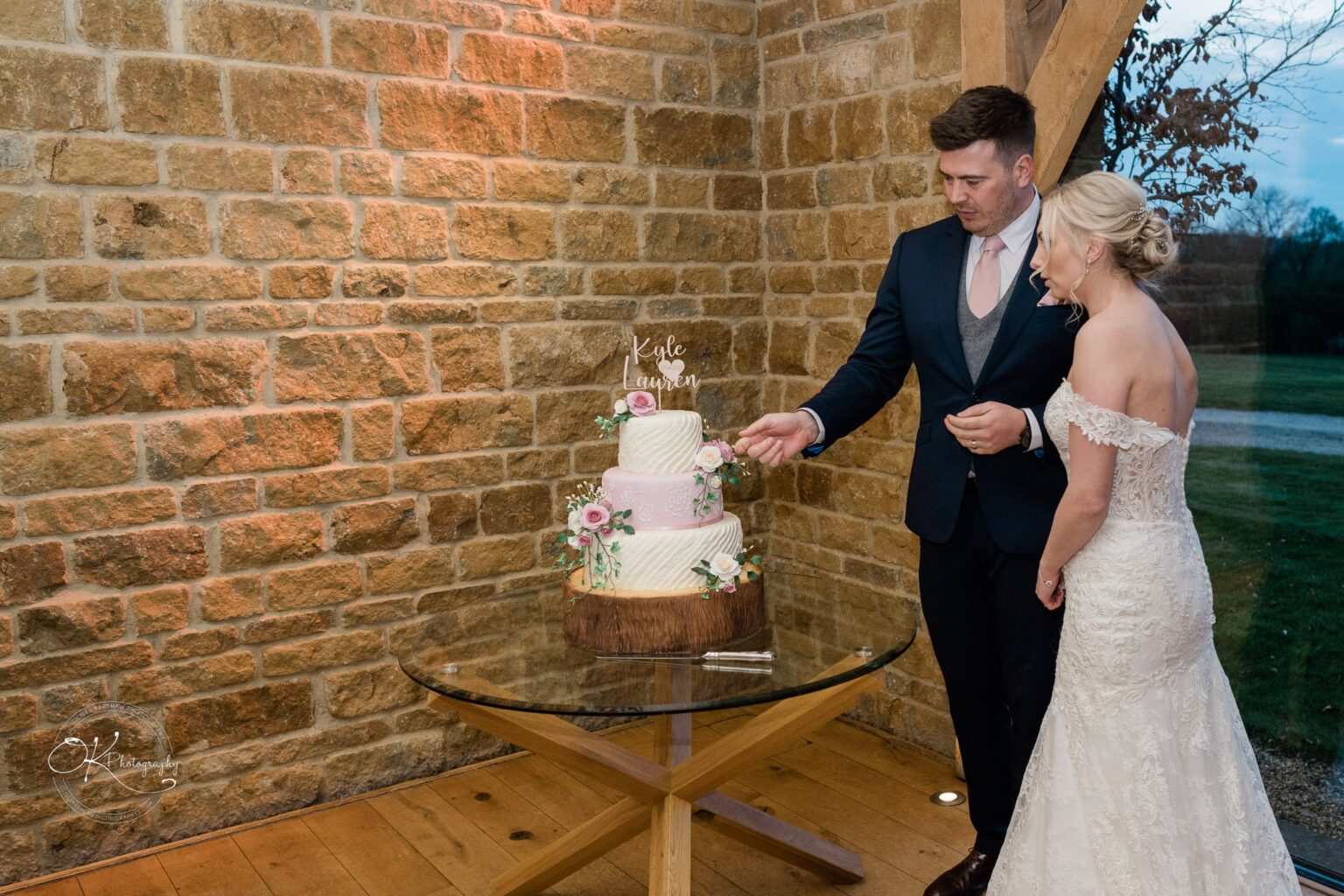 Dodford Manor Barn Wedding Photography A bride and groom cutting their wedding cake in front of a stone wall at Dodford Manor Barn.