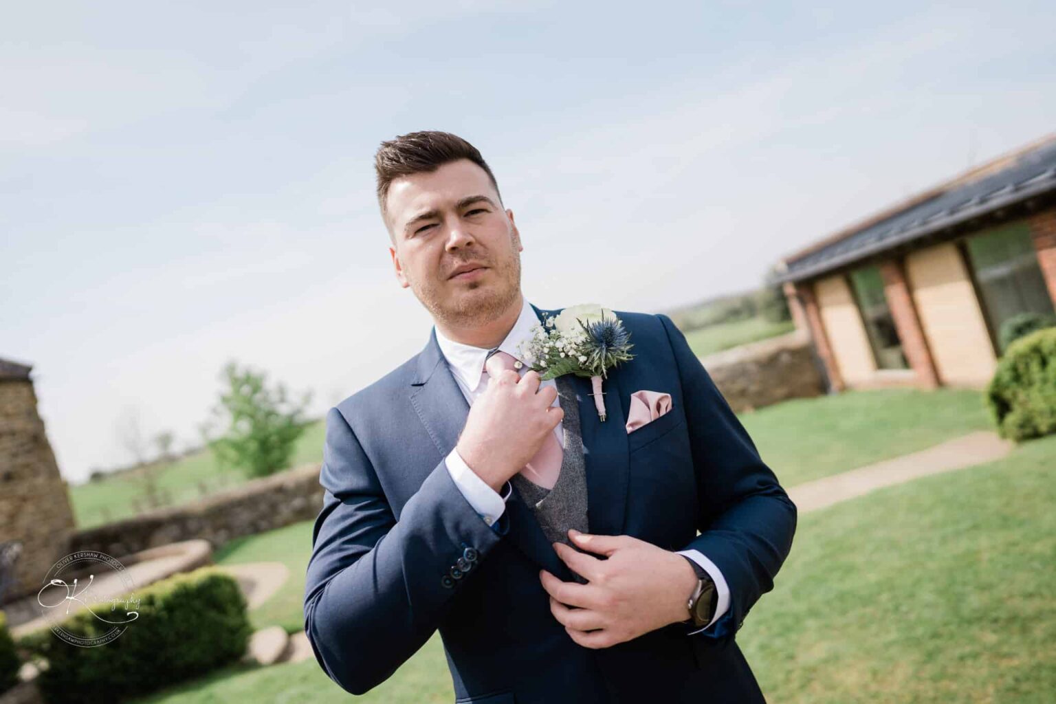 Dodford Manor Barn Wedding Photography Man in a navy suit and pink tie standing outdoors in front of Dodford Manor Barn.