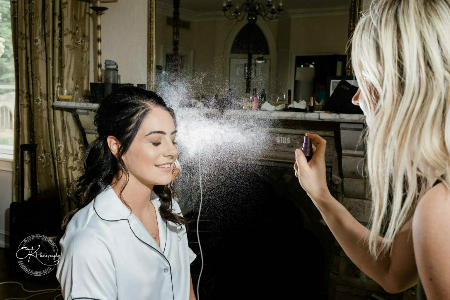 Ettington Park Hotel Wedding Photography A woman having makeup setting spray applied to her face by another person.