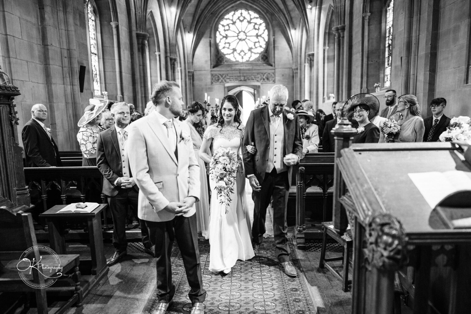 Ettington Park Hotel Wedding Photography Bride walking down the aisle with her father towards the groom in a church, surrounded by wedding guests.
