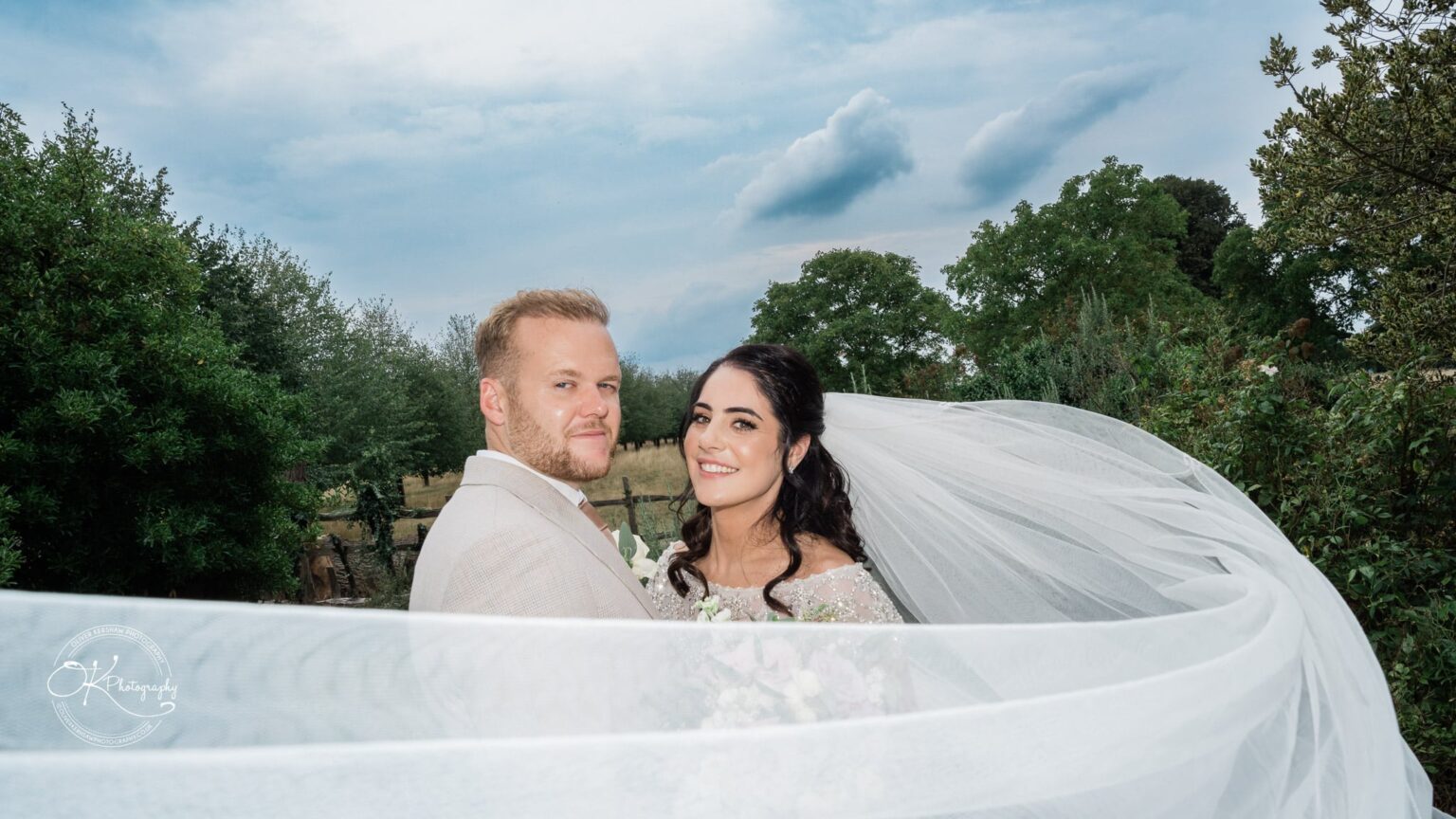 Ettington Park Hotel Wedding Photography Bride in a white wedding gown and veil with groom in a beige suit standing close together outdoors, both smiling at the camera.