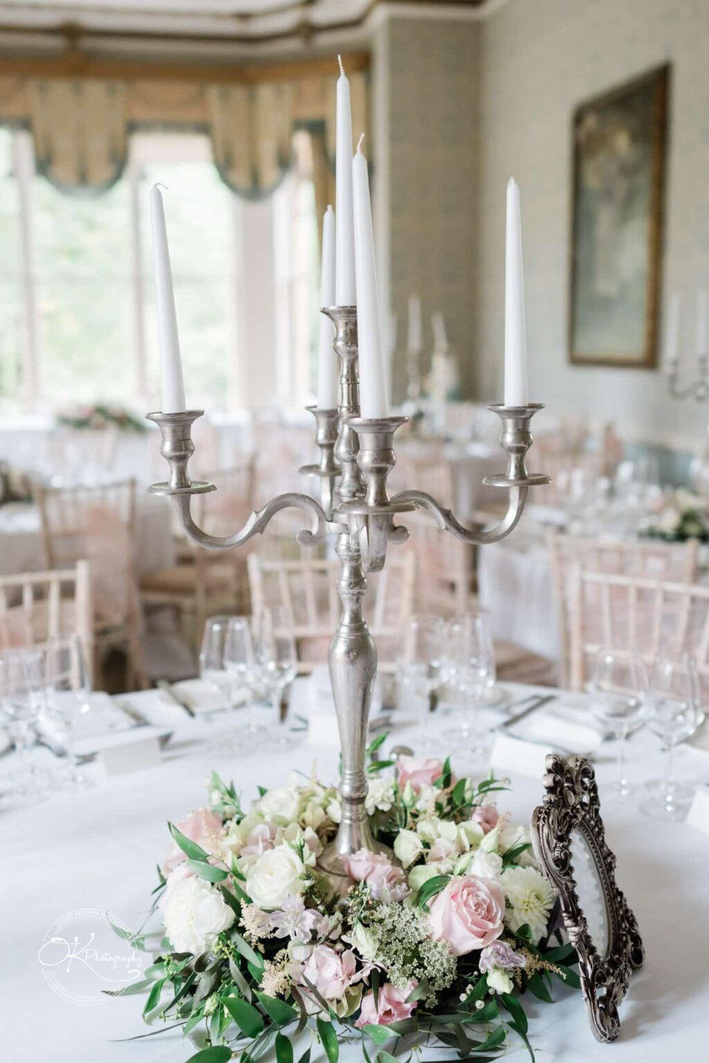 Ettington Park Hotel Wedding Photography Ornate silver candelabra with white candles surrounded by a floral arrangement of white and pink roses on a elegantly set table.