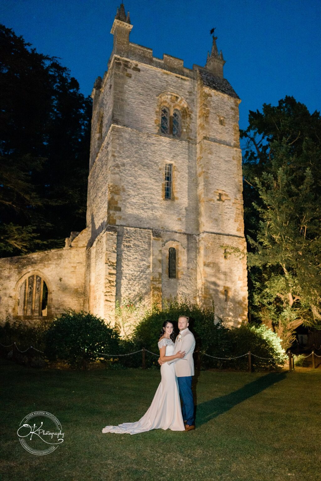 Ettington Park Hotel Wedding Photography A couple in formal attire poses in front of a lit, historic stone building at night.