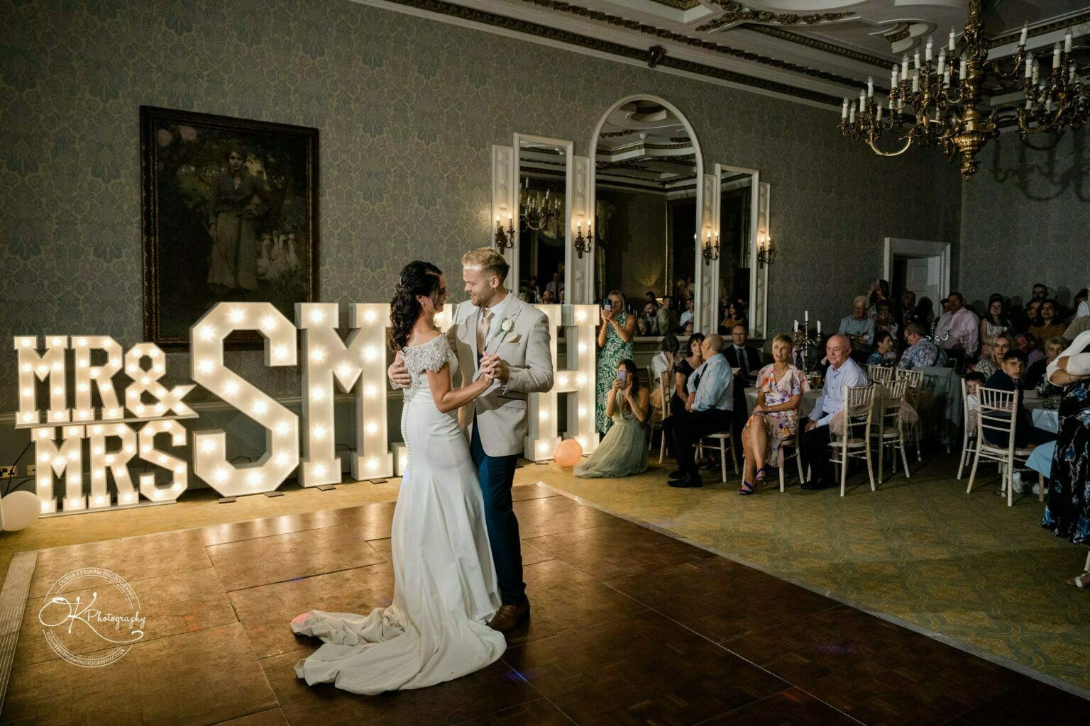 Ettington Park Hotel Wedding Photography Bride and groom dancing in an elegant reception room with large illuminated "Mr & Mrs Smith" sign.